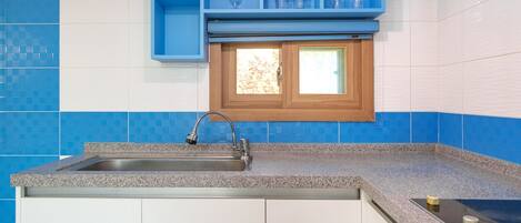A kitchen with a granite countertop, a stainless steel sink, and blue and white tiled backsplash.