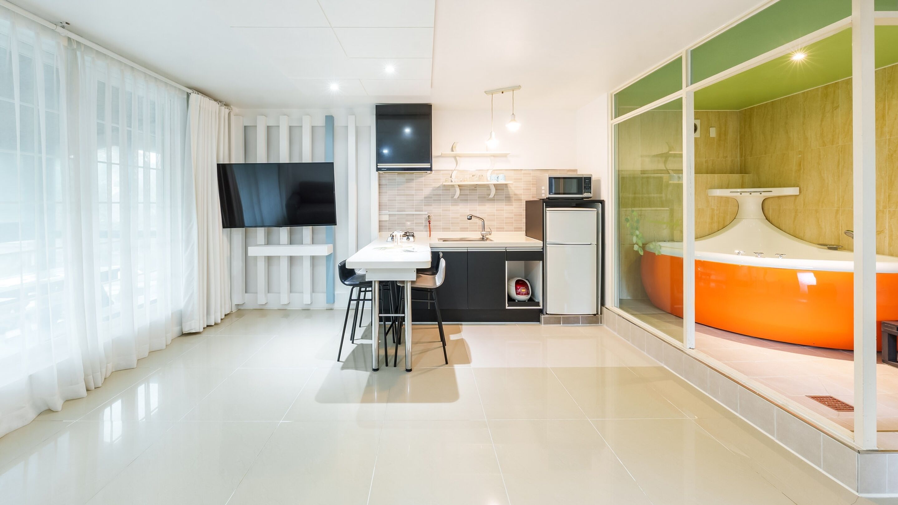 A modern kitchen with a flat-screen TV, a small refrigerator, and a sink.