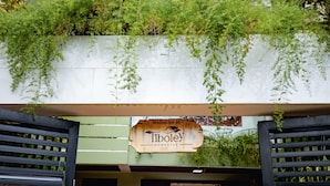 A wooden signboard with "Welcome to Tiboley Homestay" written on it, hanging above a doorway with a black frame.