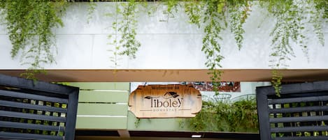 A wooden signboard with "Welcome to Tiboley Homestay" written on it, hanging above a doorway with a black frame.