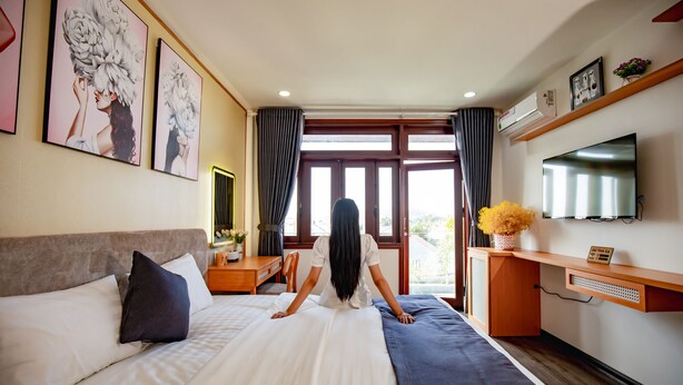 A hotel room with a bed, a desk, a TV, and large windows.