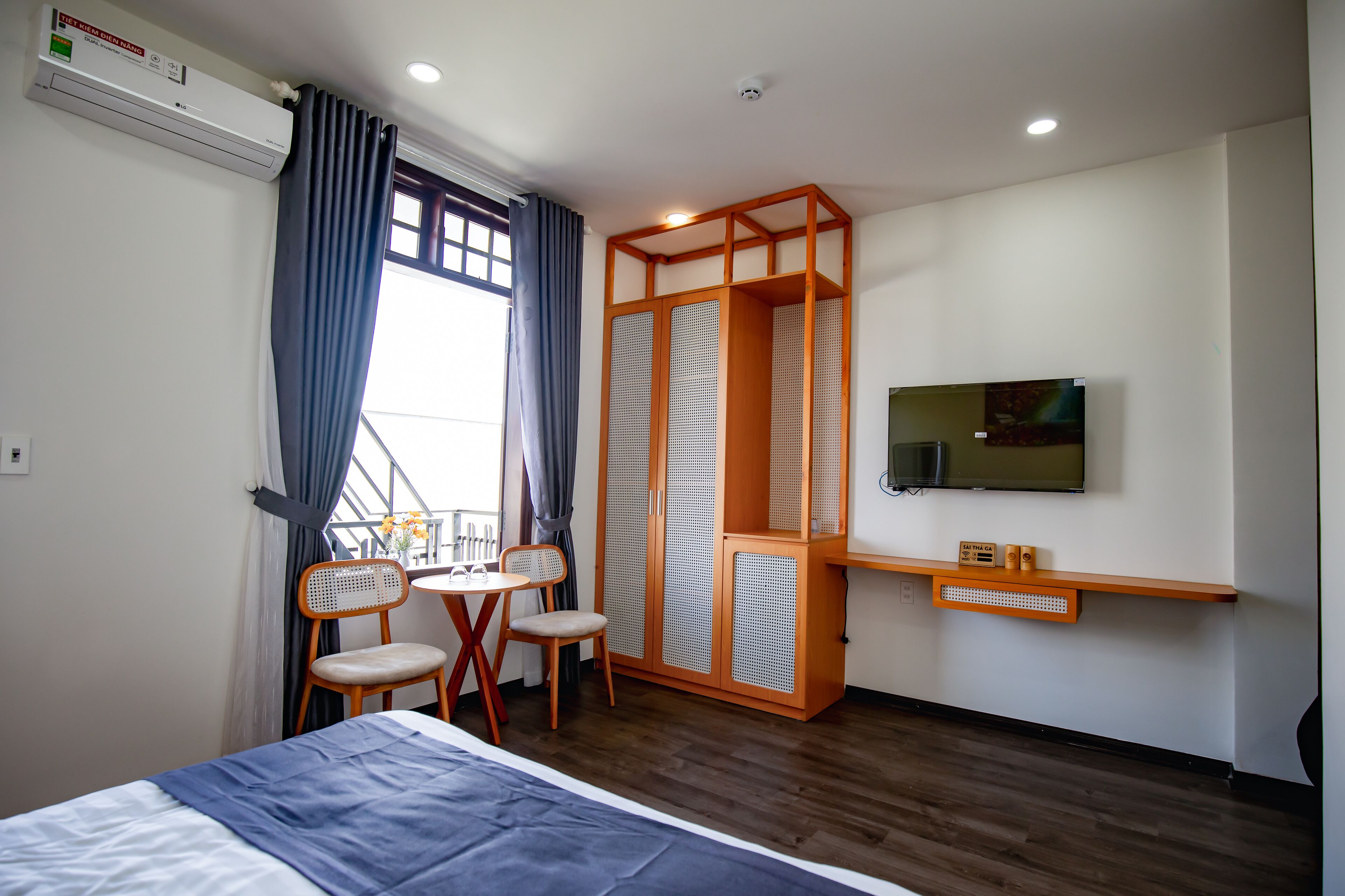Une chambre d’hôtel comprenant un lit, un téléviseur fixé au mur, une armoire en bois, une petite table avec des chaises et un appareil de climatisation.