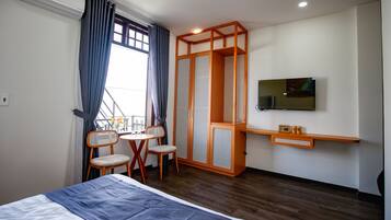 Une chambre d’hôtel comprenant un lit, un téléviseur fixé au mur, une armoire en bois, une petite table avec des chaises et un appareil de climatisation.