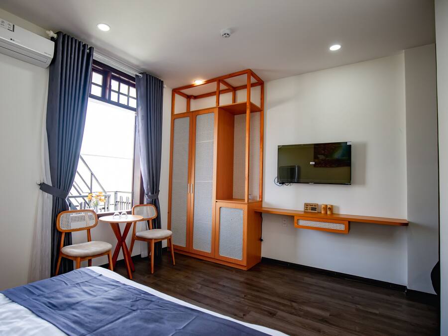 Une chambre d’hôtel comprenant un lit, un téléviseur fixé au mur, une armoire en bois, une petite table avec des chaises et un appareil de climatisation.