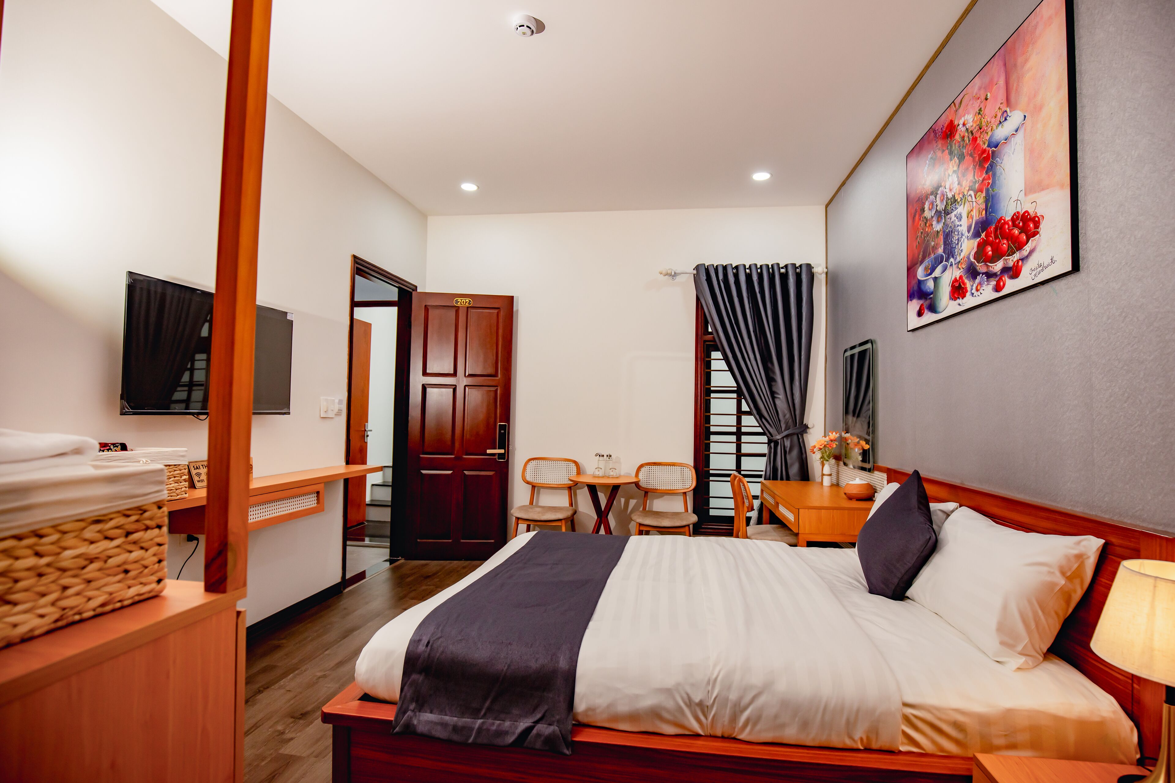 A hotel room with a bed, a desk, a chair, a television, and a painting on the wall.