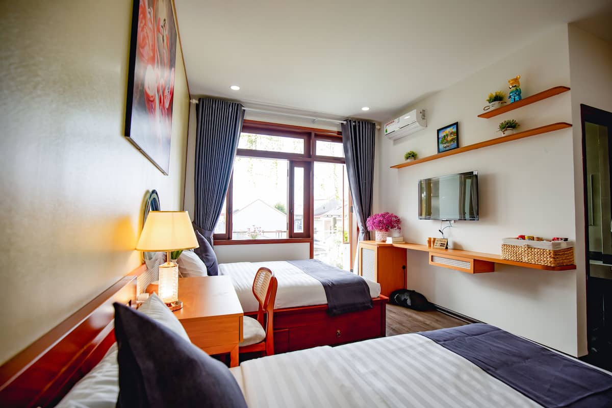 Une chambre d’hôtel avec deux lits, un bureau, une chaise, une lampe, une télévision et des étagères ornées d’objets décoratifs.