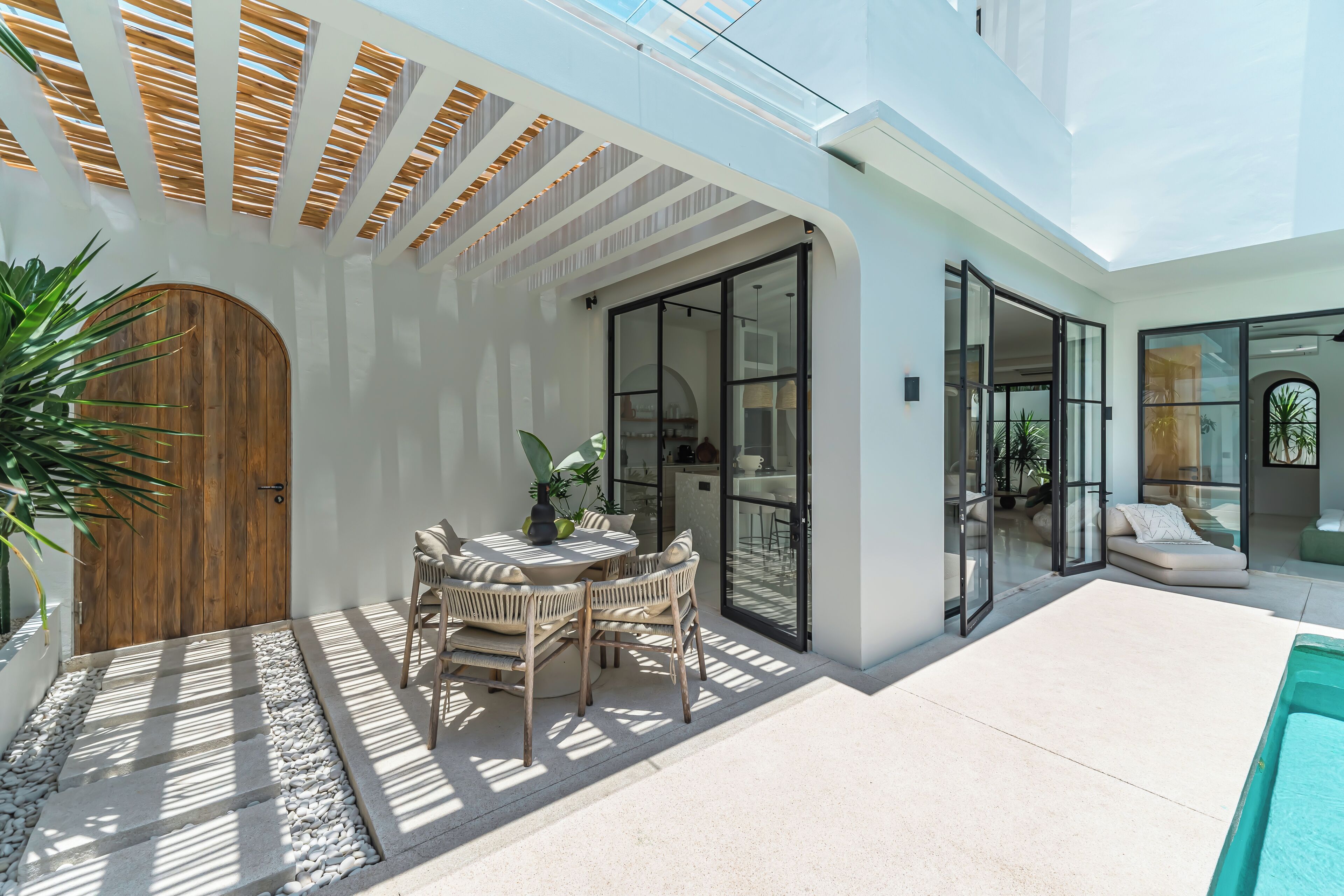 Patio esterno moderno con una porta in legno, un tavolo rotondo e sedie, e una zona piscina.