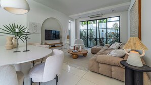 A modern living room with a round dining table, comfortable seating, a large sofa, and a television. - Sanctum house (Kerobokan)