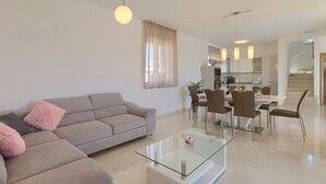 A modern living room with a sofa, a glass coffee table, and a dining area with chairs and a table. - Amazing home in Marcana (Marcana)