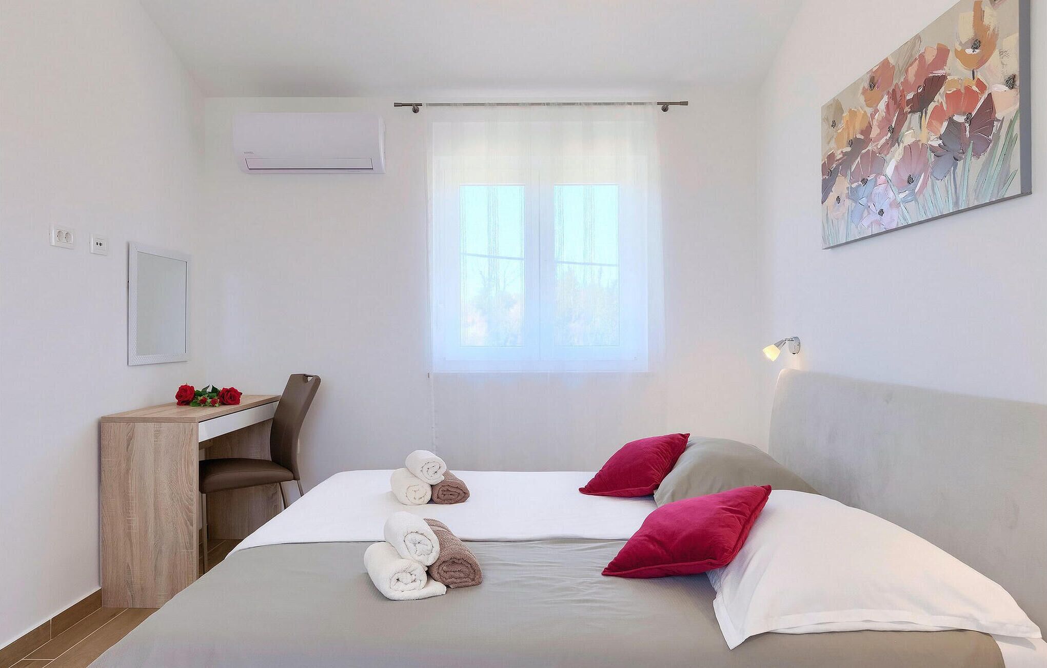 A hotel room with a bed, a desk, a chair, a mirror, and a window with curtains.