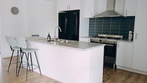 A modern kitchen with white cabinetry, a central island with bar stools, a black refrigerator, a stainless steel range hood, and a wooden floor. - Captains Edge (Paynesville)