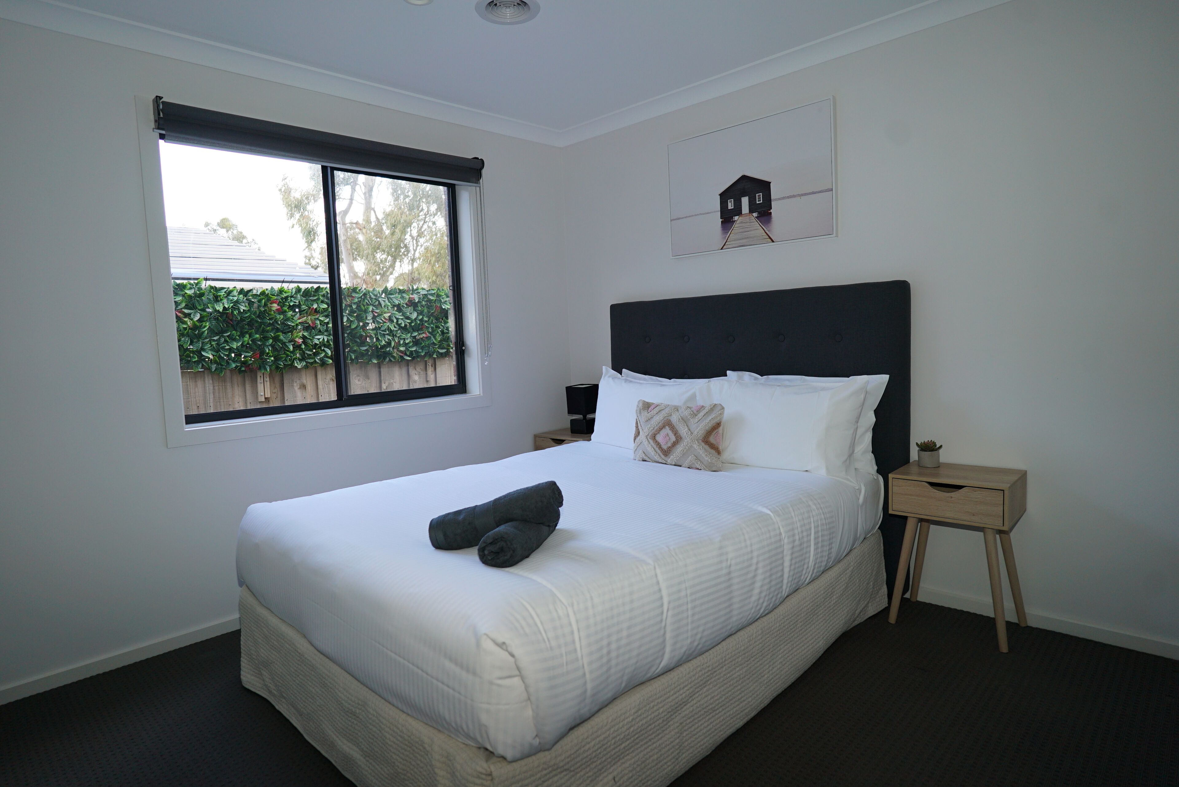 A bedroom with a large bed, a window, a nightstand, and a small plant.