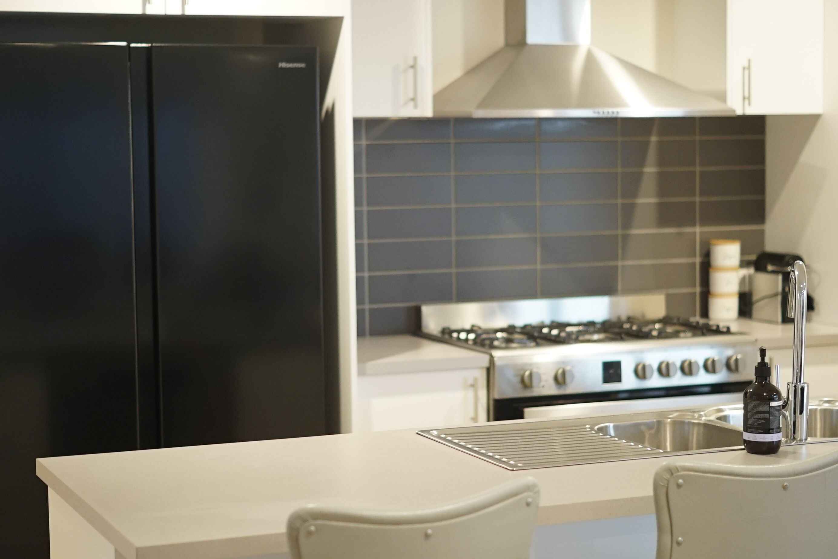 A modern kitchen with a black refrigerator, stainless steel stove, and white cabinetry.