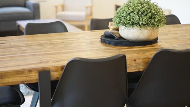 A wooden dining table with black chairs, a potted plant, and a remote control on it. - Captains Edge (Paynesville)