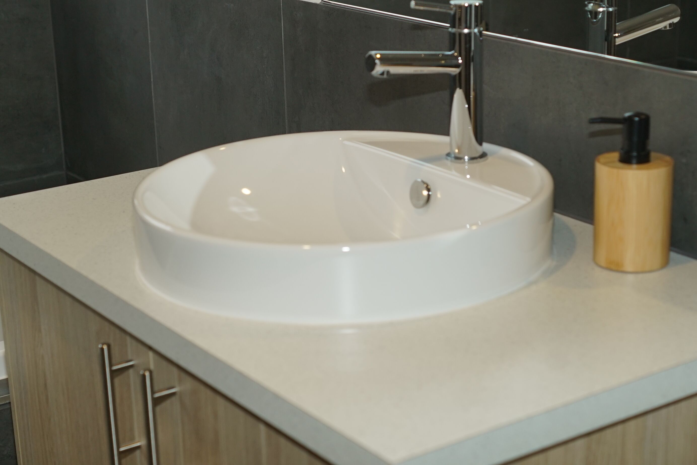 A bathroom with a white sink, a mirror, and a wooden soap dispenser.