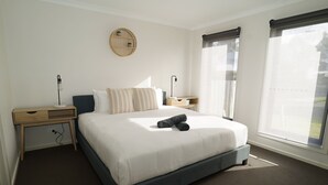 A neatly arranged hotel room with a large bed, bedside tables, a wall-mounted mirror, and a window with a view. - Captains Edge (Paynesville)