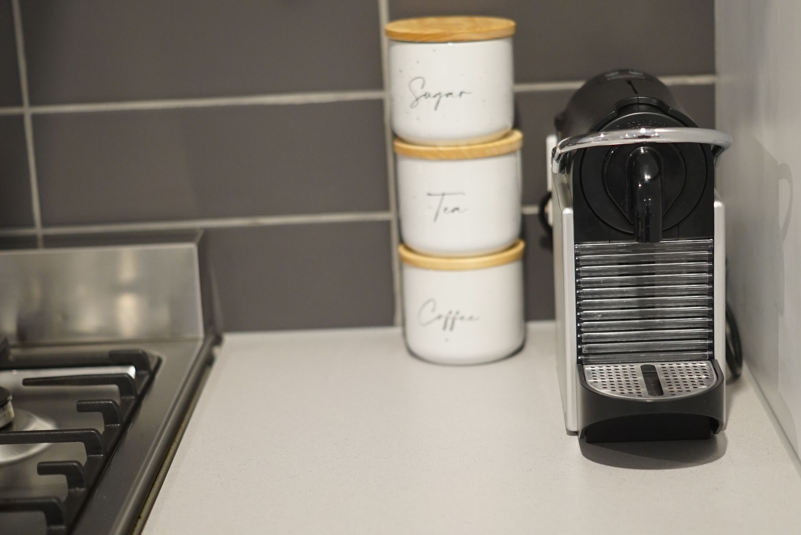 A kitchen with a stove, a coffee maker, and three stacked containers labeled "Sugar," "Tea," and "Coffee."