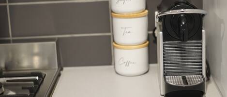 A kitchen with a stove, a coffee maker, and three stacked containers labeled "Sugar," "Tea," and "Coffee."