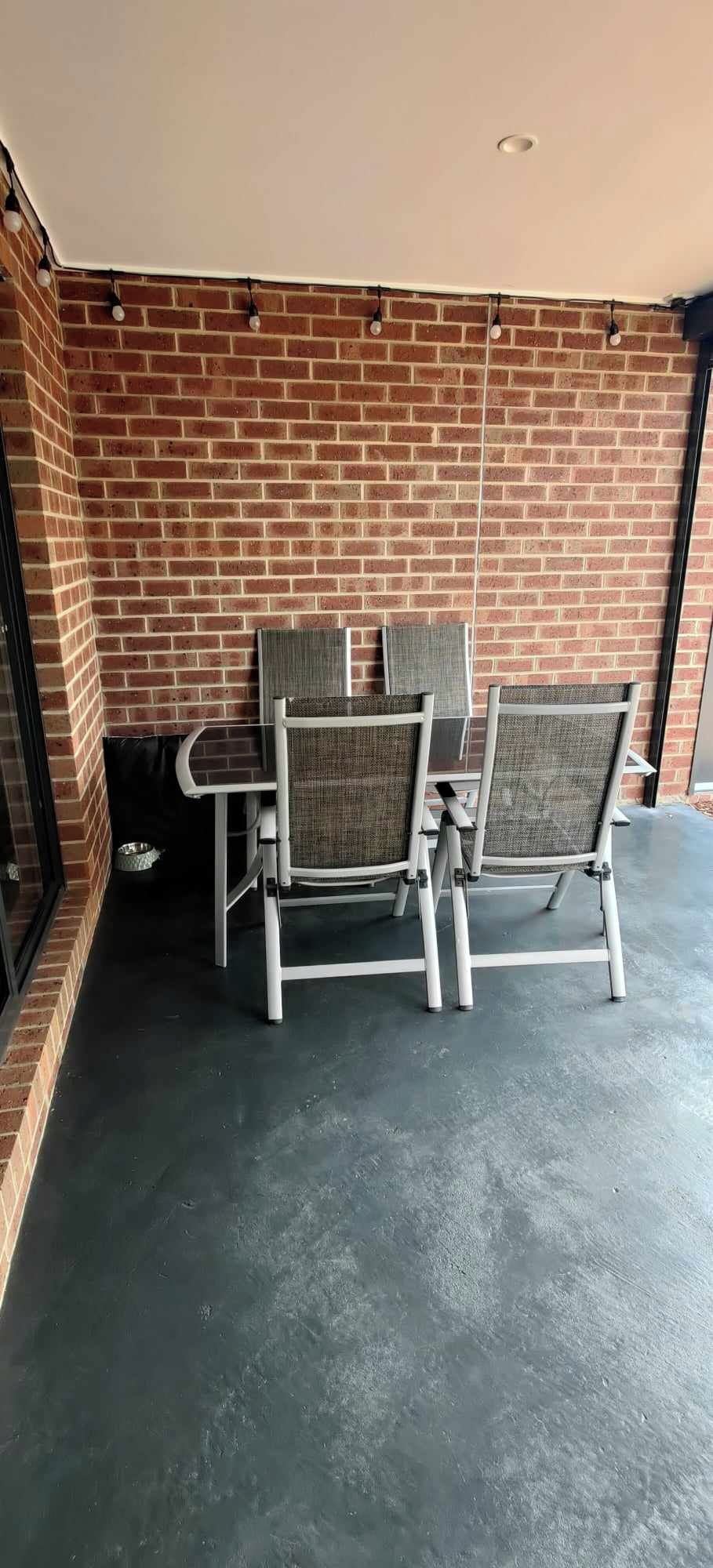 Een terras met een bakstenen muur, twee metalen stoelen en een betonnen vloer.