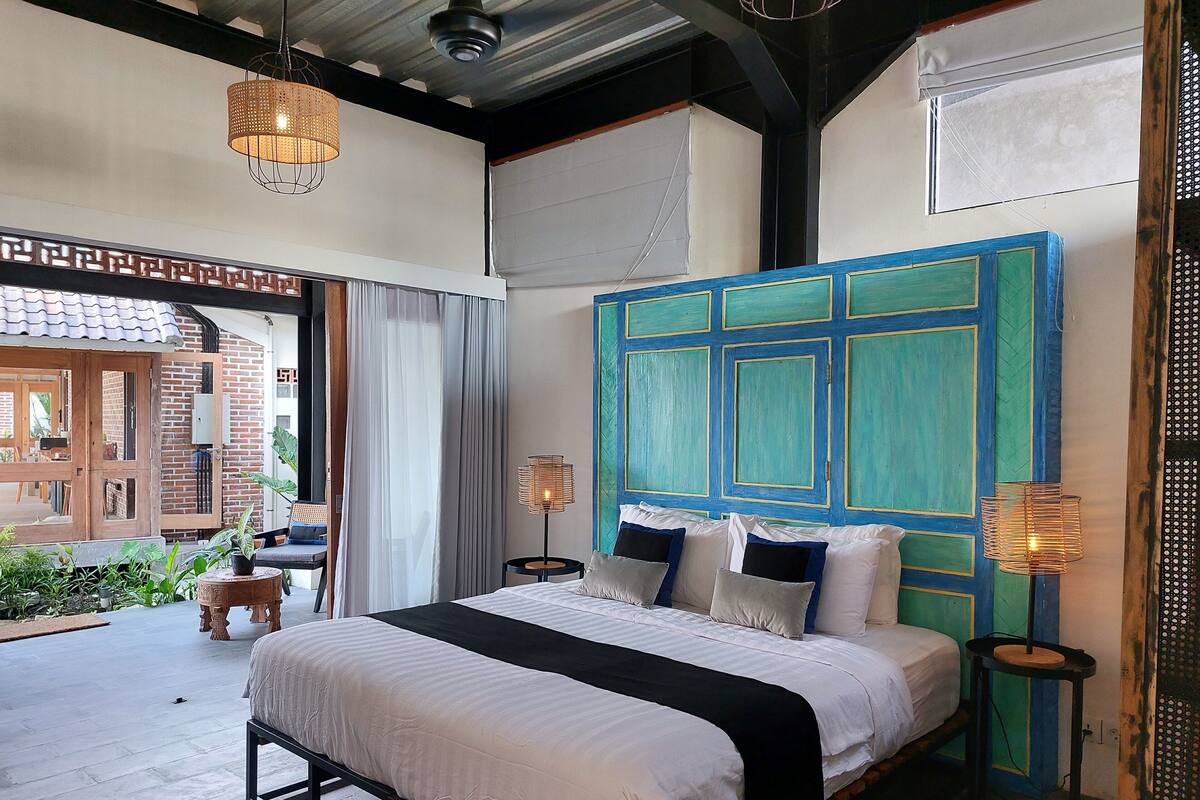 A bedroom with a bed, bedside lamps, a window with curtains, and a view of the outside.