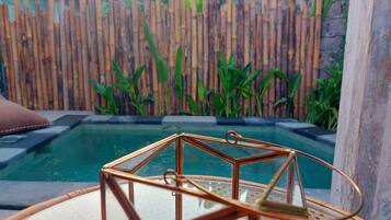 A glass-top table with a copper wireframe centerpiece, a wooden fence, and a pool in the background.