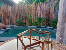 A glass-top table with a copper wireframe centerpiece, a wooden fence, and a pool in the background.
