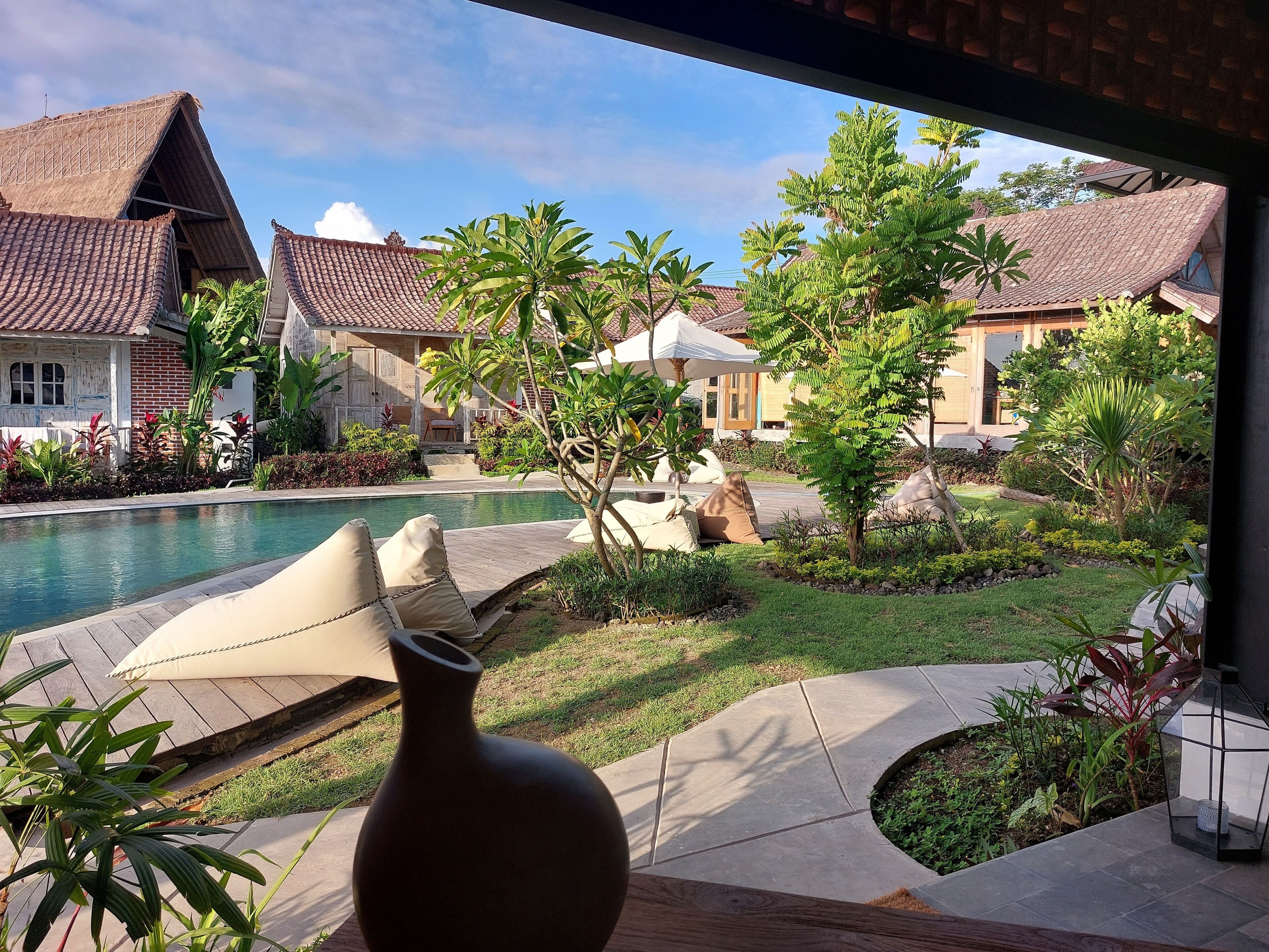 A poolside view with a lounge area, a large vase, and traditional-style buildings with tiled roofs.