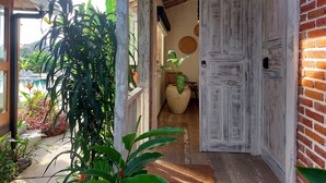 A wooden door with a rustic finish, a large potted plant, and a view of a swimming pool. - Spaces Bali (Munggu)