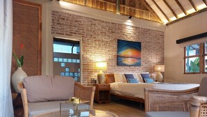 A cozy room with a brick wall, a bed with pillows, a round glass table, and a wicker chair. - Spaces Bali (Munggu)