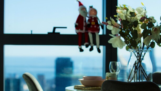 A dining area with a table set for two, a vase with flowers, and a view of the cityscape through a large window. - New Year eve’s Fireworks & BayView Apt in CBD (Melbourne)