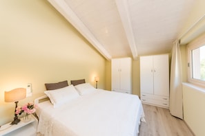 Quarto com cama, abajures, mesa de cabeceira, guarda-roupa e janela com cortinas.