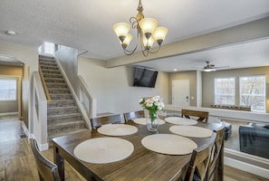 A dining area with a wooden table, woven placemats, and a vase of flowers. A staircase and a ceiling fan are visible in the background. - Tumbleweed Resort (Peyton)