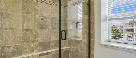 A glass-enclosed shower with beige tiles and a window with blinds.