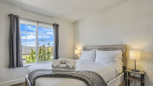 Un lit bien fait, avec une serviette pliée, une lampe de chevet et une vue sur la verdure par la fenêtre.