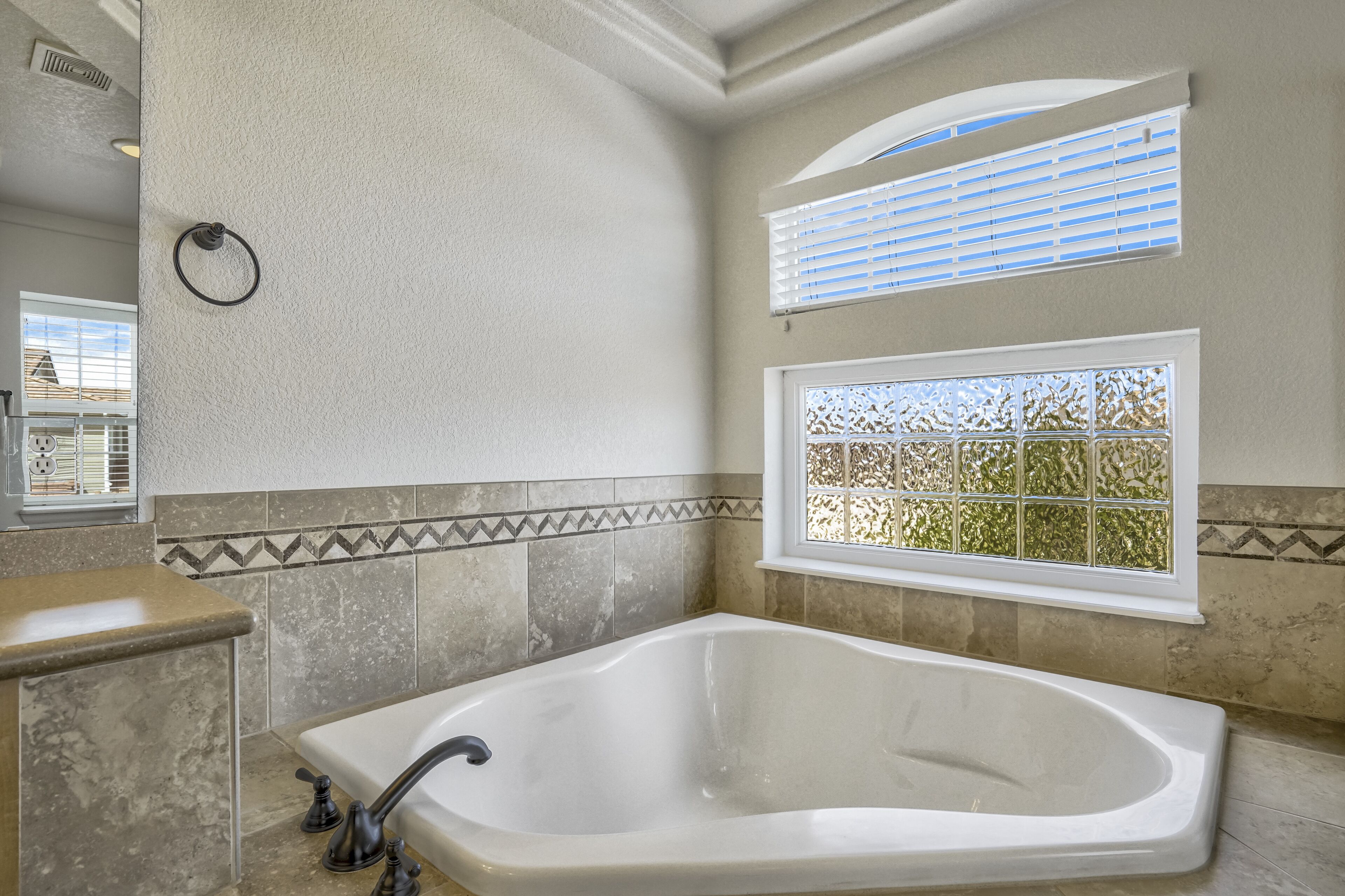 A bathroom with a freestanding bathtub, a window with blinds, and a decorative tile border.
