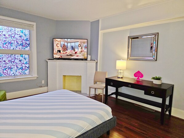 Un dormitorio con cama, chimenea, televisor, escritorio y espejo.