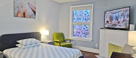 Un dormitorio moderno con una cama, un sillón verde, una chimenea y un televisor mostrando un paisaje navideño.
