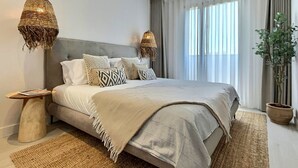 Ein modernes Schlafzimmer mit einem großen Bett, zwei Pendelleuchten, einem Nachttisch und einem Blumentopf.