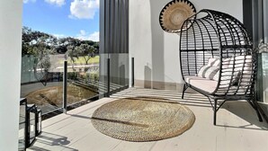 Ein Balkon mit einem gewebten Teppich, einem schwarzen Drahtstuhl und einer dekorativen Platte an der Wand.