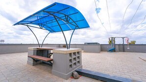 Una terraza en la azotea con un toldo azul, un banco de hormigón y una mesa de piedra.