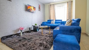 Un salón con un sofá azul, una mesa de centro y un televisor montado en la pared.