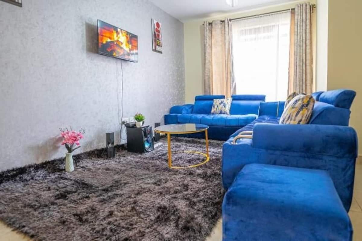 A living room with a blue sofa set, a coffee table, and a TV mounted on the wall.