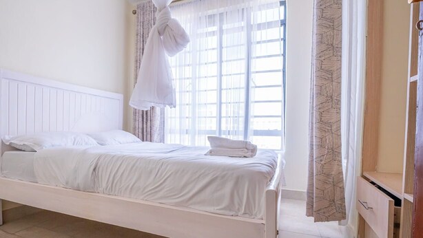 Habitación individual con una cama y cabecera blanca, una ventana con cortinas traslúcidas y un armario de madera.