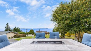 Un patio exterior con una mesa dispuesta para cuatro personas, con vistas a un paisaje marino y una zona residencial.