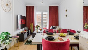 A modern living room with a flat-screen TV displaying 'Netflix', a dining area with red chairs, and a view of a building through large windows. - Lumina apart near Michał Klepacz Park (Lodz)