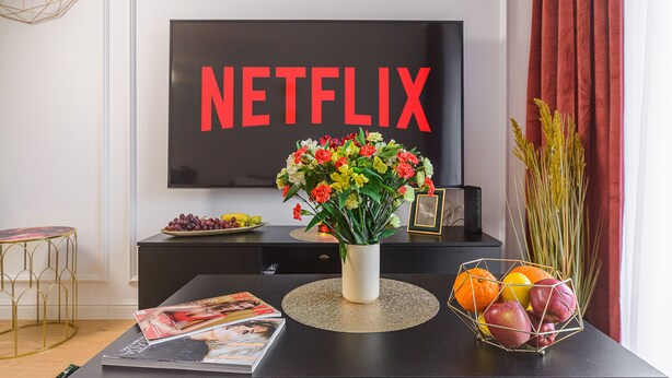 A living room with a TV displaying "NETFLIX," a vase with flowers, a fruit bowl, and a magazine on a table. - Lumina apart near Michał Klepacz Park (Lodz)