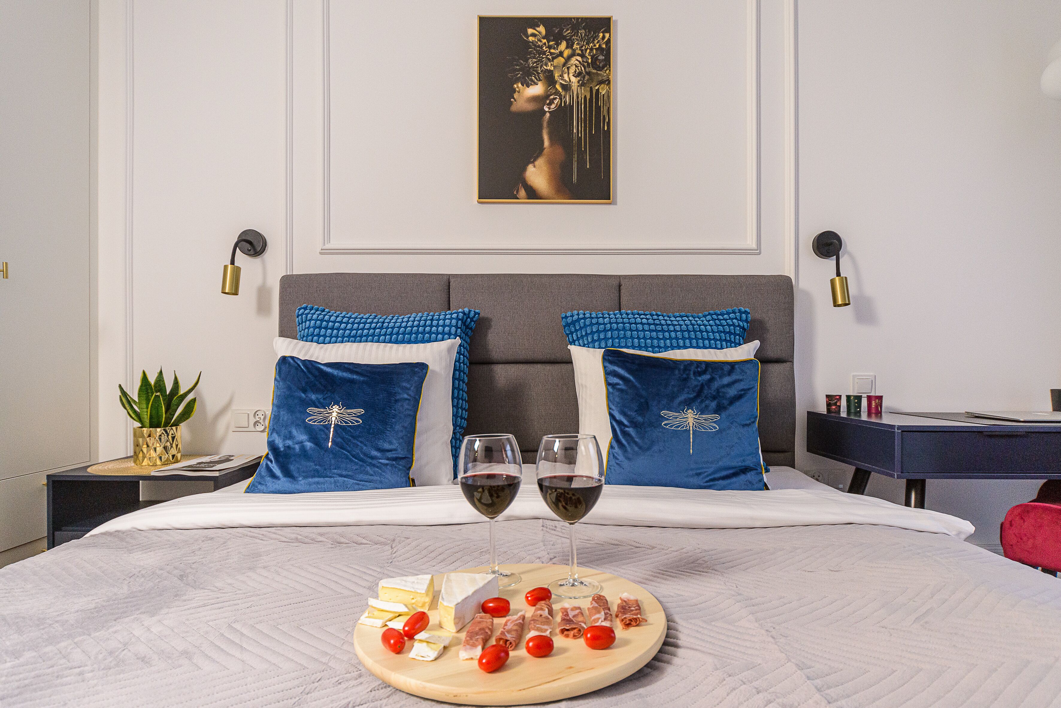 A neatly made bed with a decorative pillow, a bedside table with a plant, and a framed artwork on the wall.