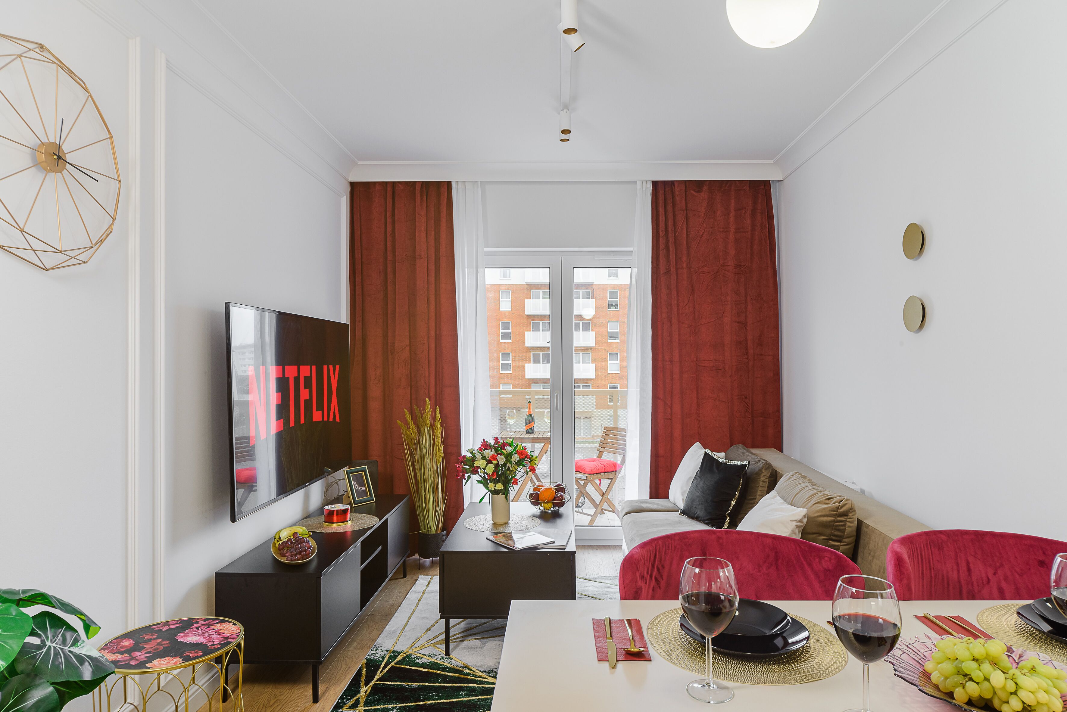 Una sala de estar moderna con un televisor de pantalla plana, una mesa de comedor para dos personas y un sofá con cojines rojos.