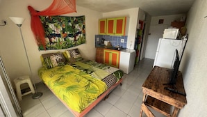 A compact bedroom with a bed, a small kitchenette, and a TV. - Studio tout confort dans son écrin de verdure au pieds de la Marina (Saint-François)