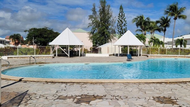 A swimming pool with a tiled deck, two white gazebos, and palm trees in the background. - Studio tout confort dans son écrin de verdure au pieds de la Marina (Saint-François)